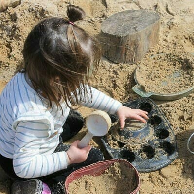 Girl making sand sculptures with metal trays